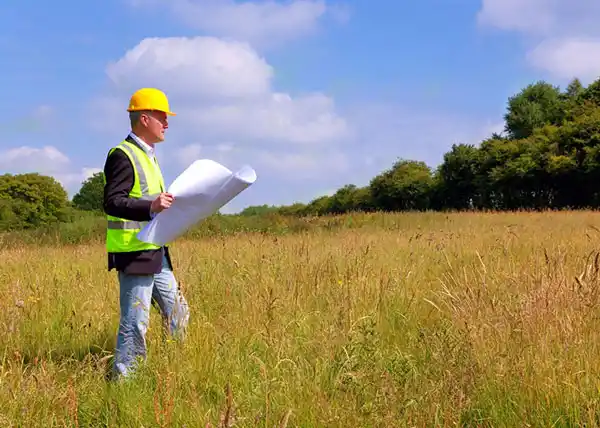 Surveyor Holding Plans Standing in Raw Farmland